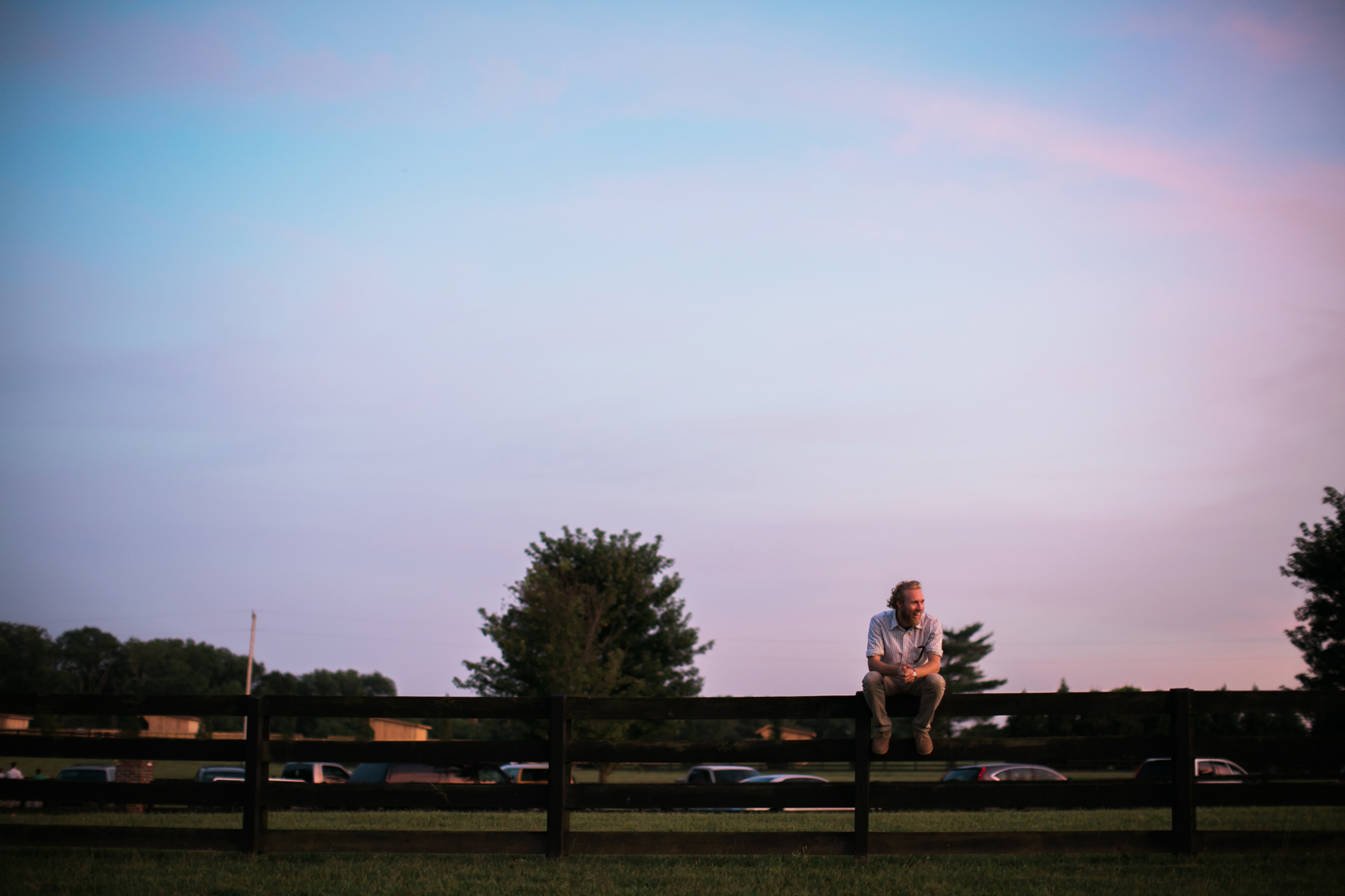 Man sitting on fence at sunset